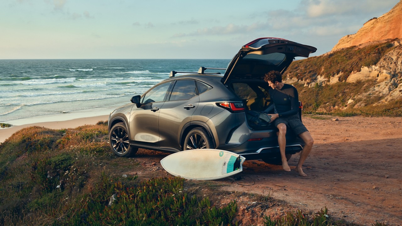 A man sat on the boot of the Lexus NX on the coast