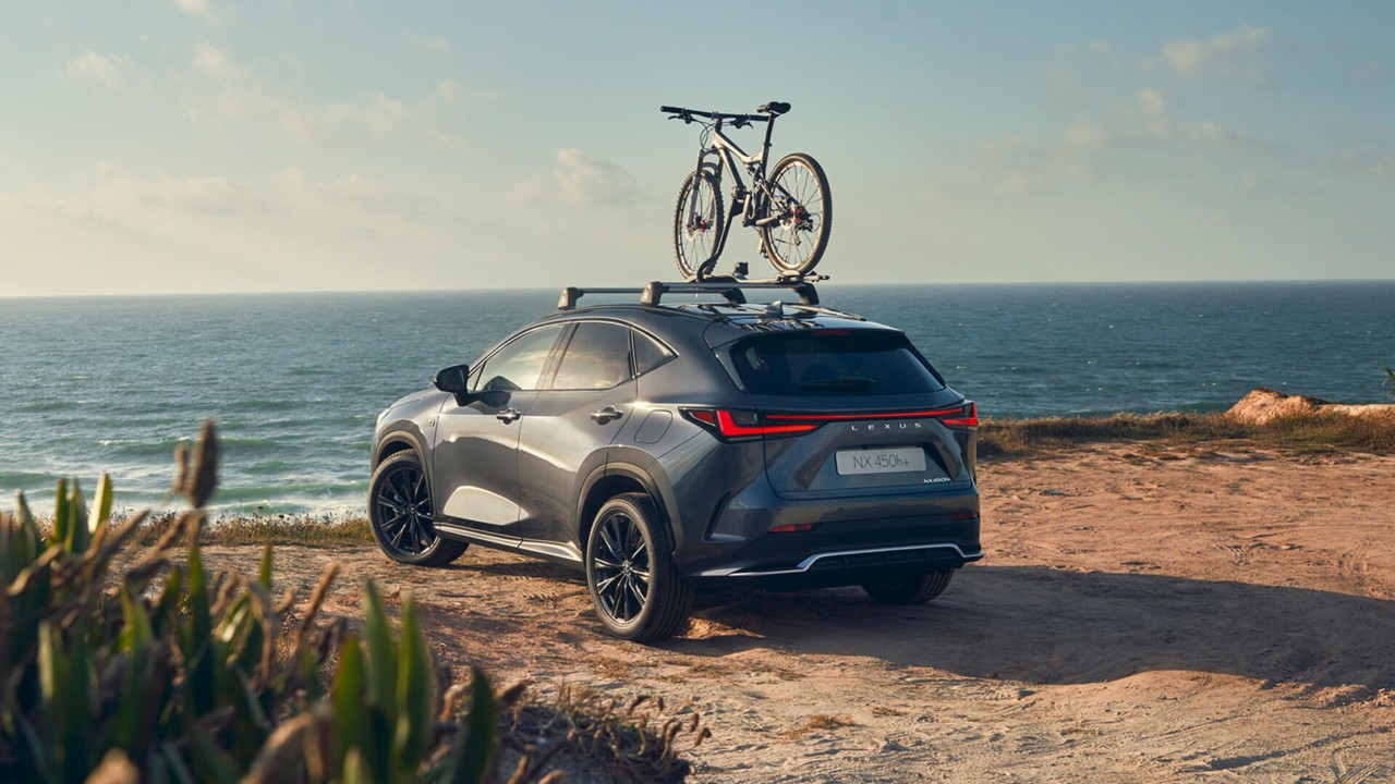 A Lexus NX 450h+ with a bicycle on it's roof rack at a coastal location