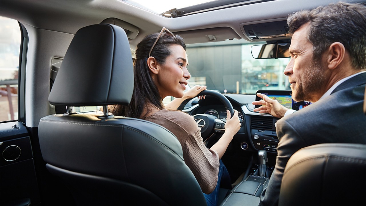 A man and woman driving a Lexus across a bridge